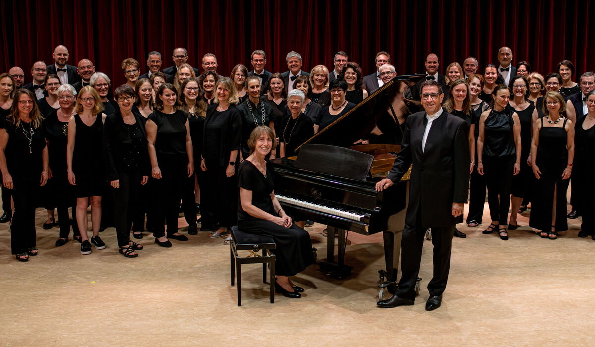 Gemischter Chor mit Dirigent sowie Begleitung am Flügel vor der Bühne